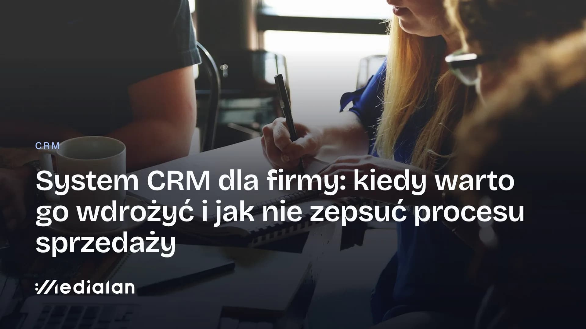 Zespół przy wspólnym stole notuje w zeszytach podczas spotkania, obok laptopy i kubek kawy